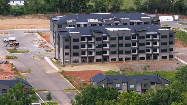 A four story apartment block nears completion beside new townhomes and empty parking lots on red Virginia clay at a Lynchburg housing development. Aerial approaching shot