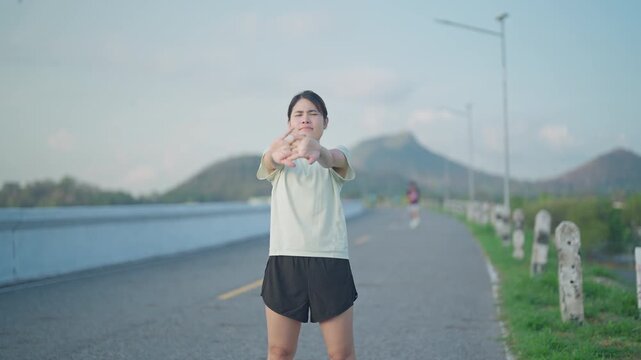 Young Asian woman warming up and stretching her muscles before jogging in the park. Female athlete getting ready for running workout in morning. Fitness, wellness and work life balance concepts