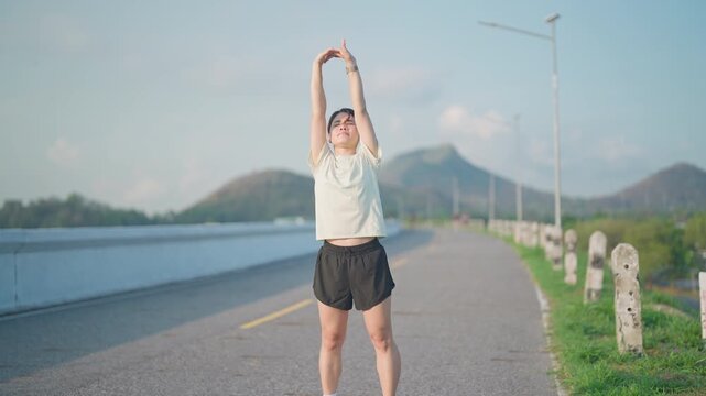 Young Asian woman warming up and stretching her muscles before jogging in the park. Female athlete getting ready for running workout in morning. Fitness, wellness and work life balance concepts