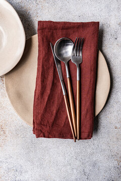 Rustic table setting with copper cutlery and burgundy napkin