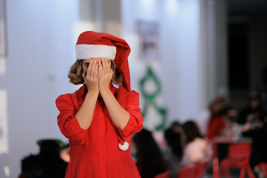 Sad Woman In Santa Hat Covering Her Face At Christmas Party. Unhappy lady wearing red festive clothing hides behind hands during winter event 
