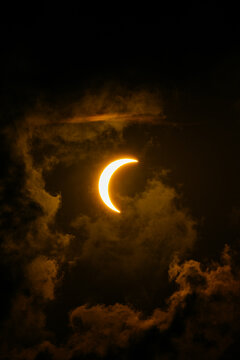 Solar eclipse crescent glow through dramatic dark cloudscape