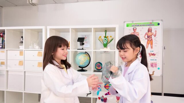 Two Schoolgirls in Lab Coats Playing with Spring Toy in Classroom