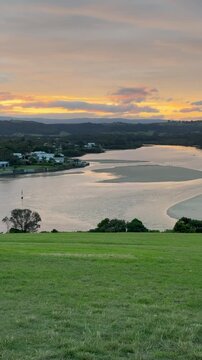 A girl stands on the grassy meadow admiring a stunning orange sunset over the bay at Minnamurra Lookout, near Jervis Bay, Wollongong and Kiama, New South Wales, Australia.