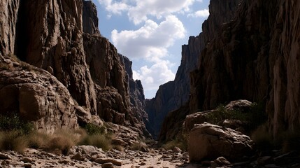 Obraz premium A narrow canyon with towering rocky walls and a clear blue sky with scattered clouds above