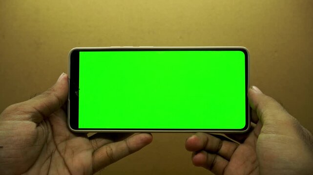 Close up of hands holding modern smartphone with empty blank green screen display for chroma key editing or app marketing template mockups in studio setting