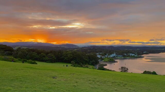 A panoramic view of a stunning orange sunset over a meadow and bay at Minnamurra Lookout, Killalea Regional Park, near Wollongong and Kiama, New South Wales, Australia.