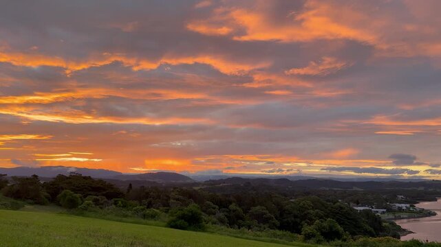 A panoramic view of a stunning orange sunset over a meadow and bay at Minnamurra Lookout, Killalea Regional Park, near Wollongong and Kiama, New South Wales, Australia.