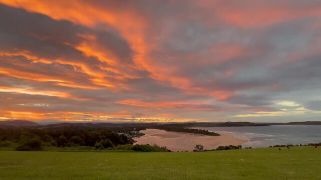 A panoramic view of a stunning orange sunset over a meadow and bay at Minnamurra Lookout, Killalea Regional Park, near Wollongong and Kiama, New South Wales, Australia.