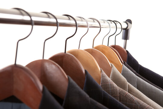 Close up perspective of men suit jackets and blazers hanging on wooden hangers on metal rack against white background.