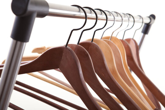 Close up perspective of empty wooden hangers hanging on metal garment rack against white background.