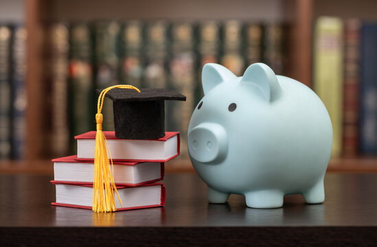 A conceptual image representing the cost of education, science funding, and financial literacy, featuring an academic cap, a books and a piggy bank