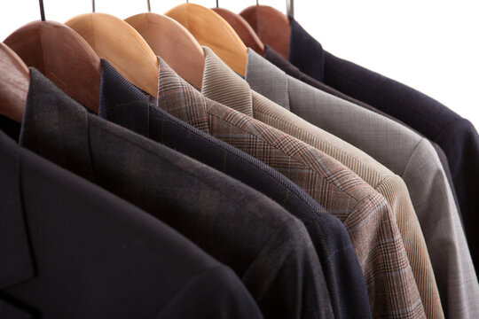 Row of classic men jackets and suits hanging on wooden hangers in closet or retail store.