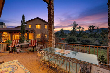 Obraz premium Sunset patio with stone columns, warm lights, glass tables, and outdoor seating overviews hills wide