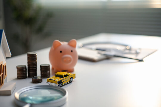 House, toy car, piggy bank and coins illustrate insurance comparison. A magnifying glass and clipboard represent evaluating home and auto coverage, premiums and financial protection options.