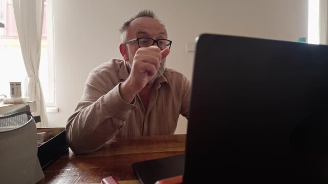 Stressed man squeezes a stress ball while working on laptop at home, showing fatigue and remote work pressure.