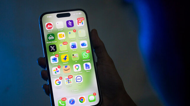 Hand holding iPhone with Google social media and messaging apps on green background.