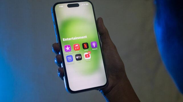 Close up of hand holding smartphone showing entertainment applications folder.