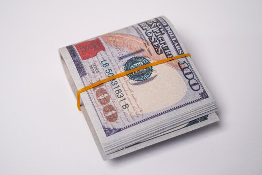 A stack of US $100 bills secured with a rubber band, set against a white background.