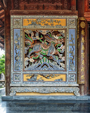 Intricate ceramic mosaic of a mythical qilin creature on a traditional wall at Tu Hieu Pagoda, Hue, Vietnam, featuring colorful tile work and elaborate wooden architectural carvings