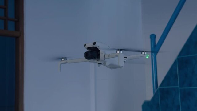 White camera drone hovering indoors for 15 seconds near blue tiled stairs and white wall. Propellers spinning with green LED. Rec.709 standard color profile. Ready to use footage for technology and ae