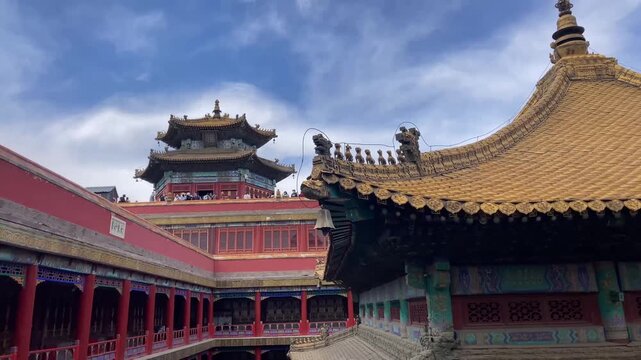 Potala Palace courtyard with golden-roofed Tibetan Buddhist temple architecture, red walls, ornate eaves, and visitors on upper balconies under blue sky