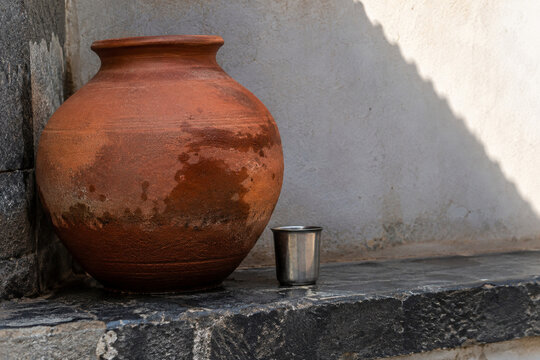 Damp Terracotta Water Jar with a Metal Cup on a Shaded Ledge