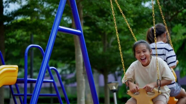 Two Asian sister girls sitting together on tandem swing having fun at outdoor playground