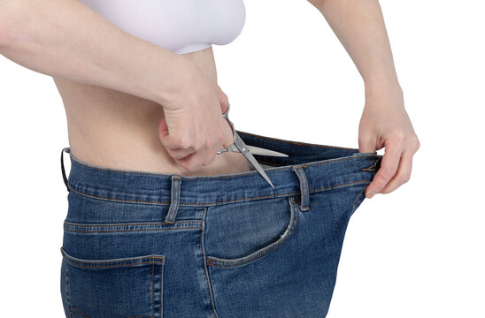 Woman cutting her oversized jeans with scissors to show weight loss result. Slim figure after diet and healthy lifestyle. Concept of body transformation and successful fitness goal