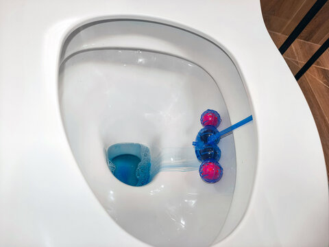 Toilet bowl rim block cleaner hanging inside white ceramic toilet. Blue liquid soap solution for disinfecting and refreshing bathroom fixture