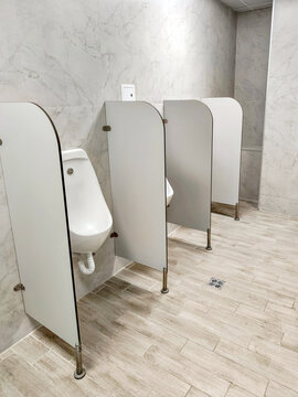 White urinal with privacy divider in commercial restroom. Modern public toilet facility with marble tiles and plumbing fixture