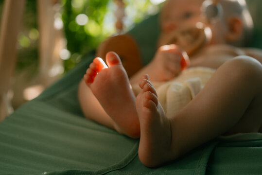 Baby feet resting in a green bouncer, soft sunlight highlighting tiny toes and new life, representing childhood, growth, and the tender beginning of human development