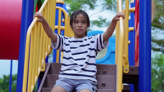 Moody Asian girl holding railing making pouting annoyed face on playground slide stairs