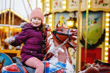 Adorable little girl riding merry-go-round carousel horse at Christmas funfair outdoors. Happy child enjoying traditional family Xmas market in Nuremberg, Germany © Irina Schmidt