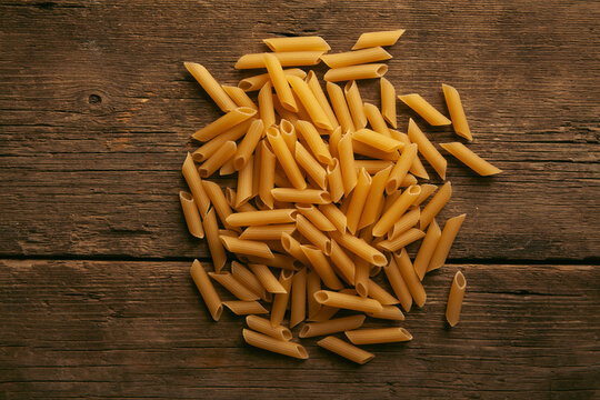 close up of penne pasta on wooden table background, top view