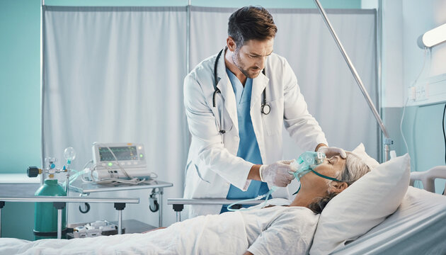 A dedicated male doctor checking a female patient lying in a hospital bed with an oxygen mask during an intensive care unit medical treatment.