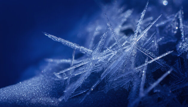 Extreme macro close up of delicate ice crystals forming intricate sharp patterns on a dark blue background during a cold winter weather day.