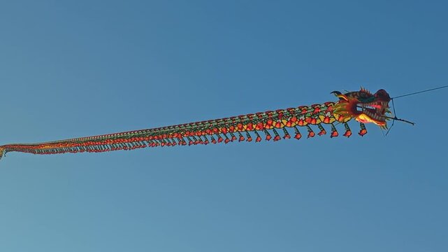 Long colorful traditional Chinese dragon kite flying in clear blue sky