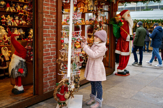 Little school girl on Christmas market. Child in a shop with Christmas tree decorations and Santa Clause figures.