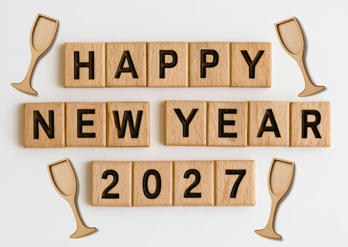 Happy New Year 2027, New Year's Eve Celebration Greeting Card - Wooden Cubes With Text And Champagne or Sparkling Wine Glasses, Isolated On White Background
