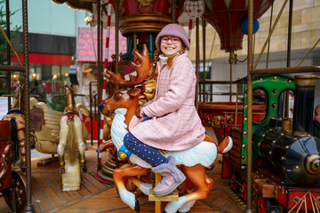 Little school girl riding on a merry go round carousel at Christmas funfair or market, outdoors. Happy child having fun on traditional family xmas market in Germany © Irina Schmidt