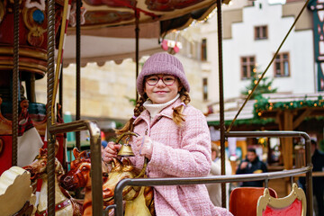 Little school girl riding on a merry go round carousel at Christmas funfair or market, outdoors. Happy child having fun on traditional family xmas market in Germany © Irina Schmidt
