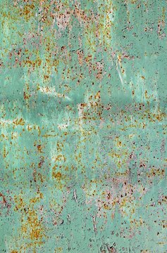 Close view of a weathered mint turquoise metal wall with peeling paint, revealing layered color transitions and an expressive aged texture.