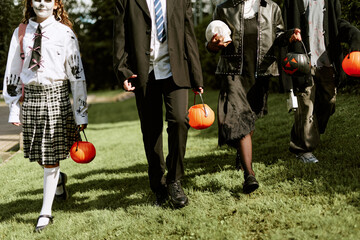 Diverse group of teenagers in costumes walking outdoors with candy buckets during Halloween. Image...
