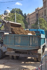 Compact loader dumping excavated soil and gravel into a dump truck during urban road reconstruction  © Анна Хмеленок