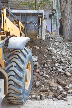 Front loader excavator parked near a pile of cobblestones and soil during urban road reconstruction
