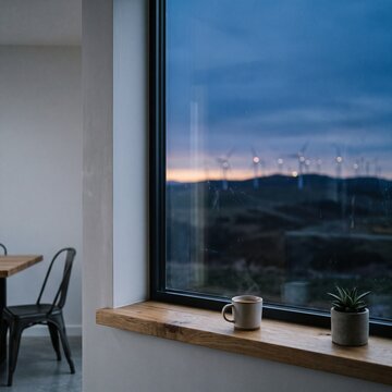 Wind turbines on a distant hill seen through a modern window at blue hour