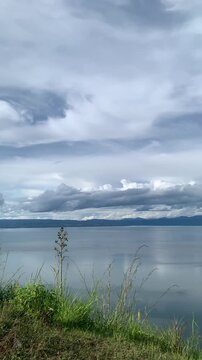 Vertical stock footage panning across the serene waters of Lake Toba from a high vantage point at Tara Bunga hill in North Sumatera, Indonesia under soft cloud daylight. Eco-tourism backdrop.