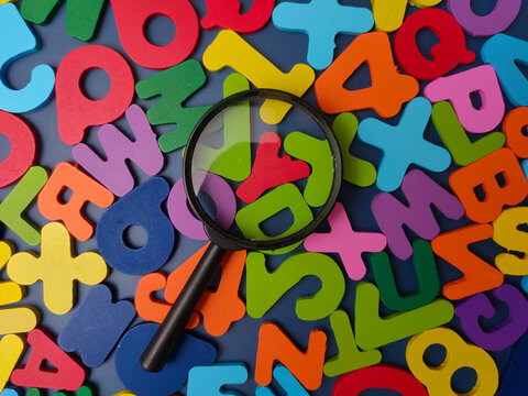 Black magnifying glass resting on a field of colorful scattered wooden alphabet letters and numbers