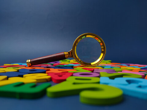 Gold magnifying glass positioned upright on a spread of colorful wooden letters and numbers under a blue backdrop
